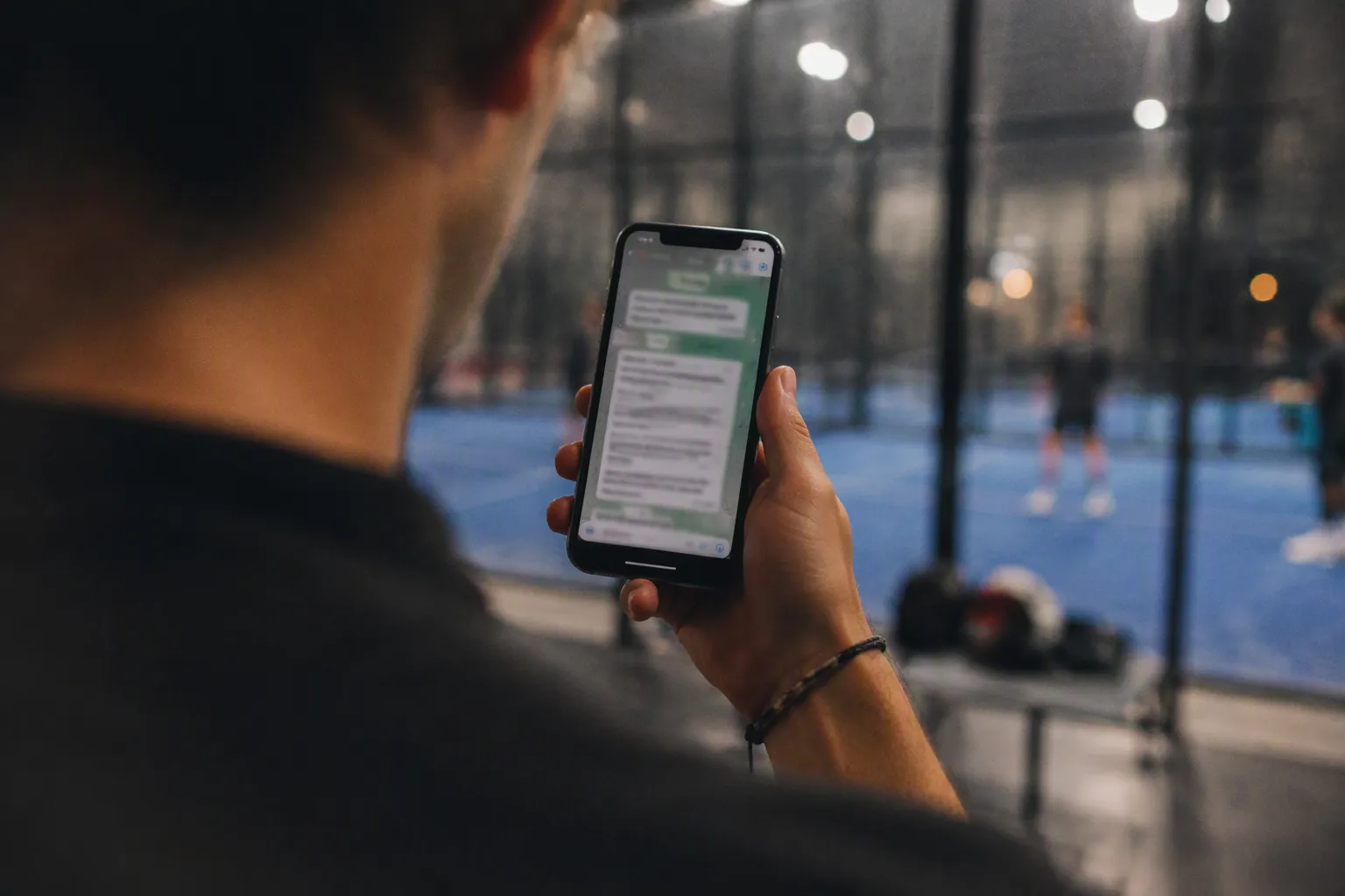 A player checks a WhatsApp group on his phone in front of a padel court